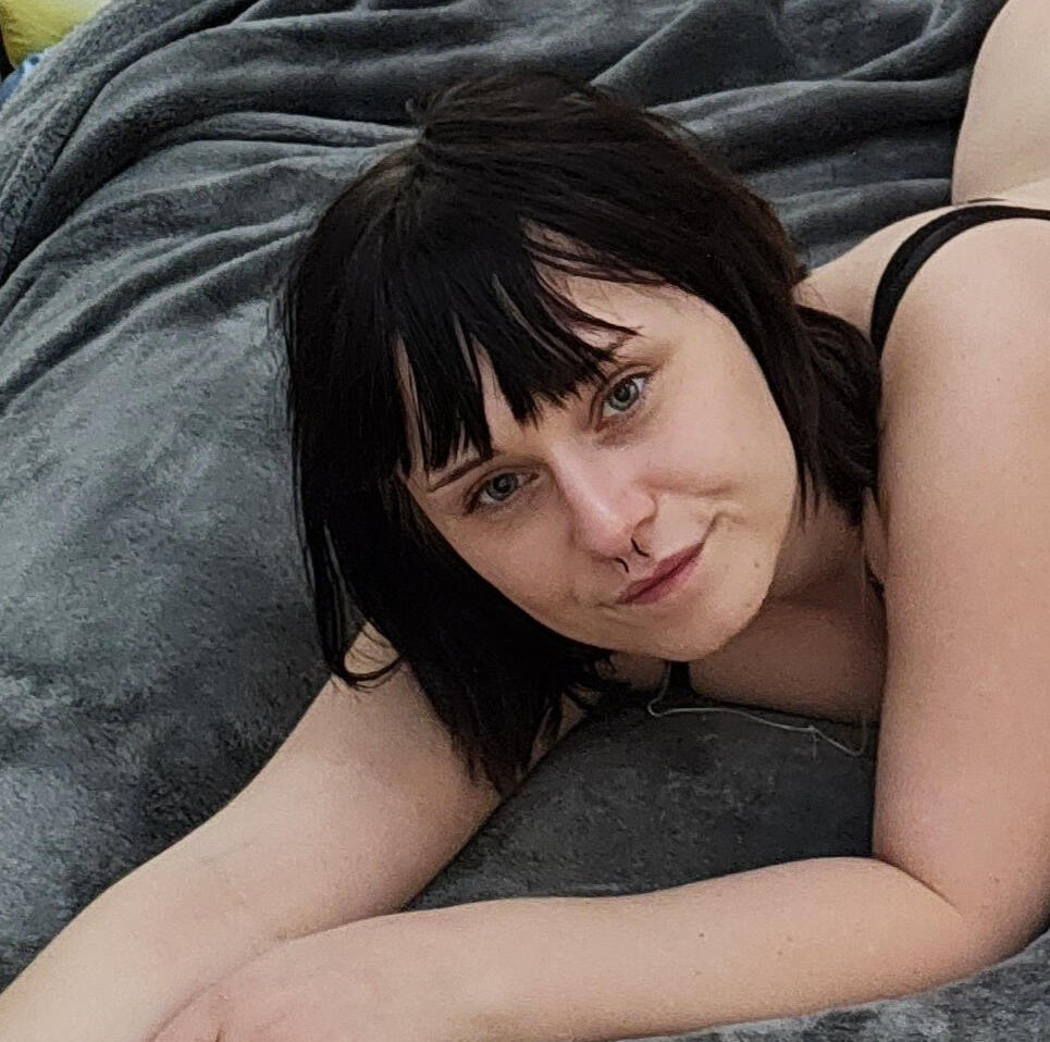 Ida Milliscent A dark haired girl lays on the bed, her face looking towards the camera.